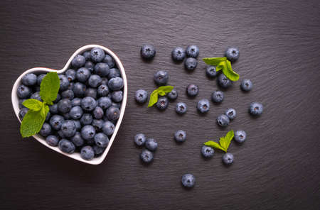 ripe blueberries lie in a bowl, heart-shaped and mint leaves, on a black backgroundの写真素材