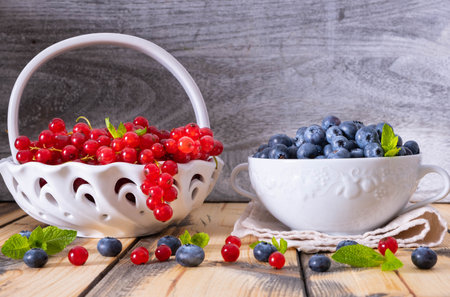 full bowls of ripe berries - blueberries, currants, and sprinkled berries and mint leaves on a wooden tableの写真素材