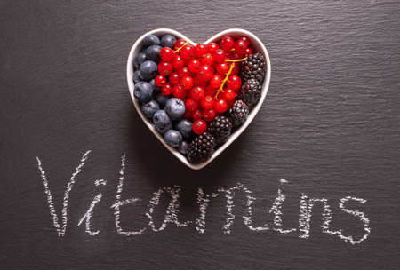 full bowl, heart shape, ripe blueberries, currants and blackberries and mint leaves and an inscription on a black backgroundの写真素材