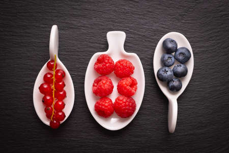 ripe berry - raspberries, red currants and blueberries, lie in a white dish on a black backgroundの写真素材