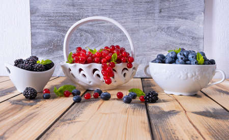 full bowls of ripe berries - blueberries, currants and blackberries, on a wooden tableの写真素材