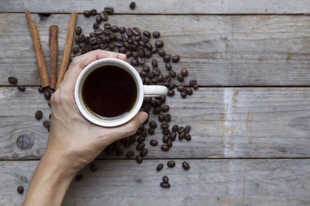 Female hands holding cup with coffee beans on wooden table backgroundの写真素材