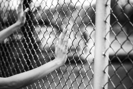 Hand holding on chain link fence, black and white conceptの写真素材
