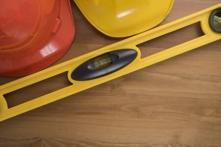 Yellow building level and helmets on the old wood table