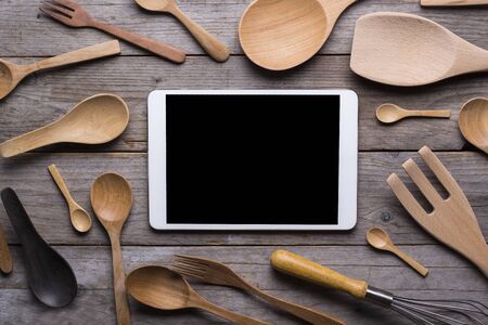 various kitchen utensils and tablet on wooden table background