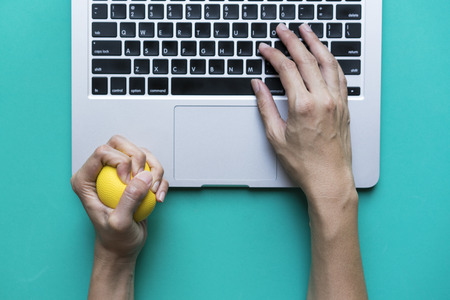 Office worker typing email on computer, feels stressed and nervous, holds a stress ball in her hand