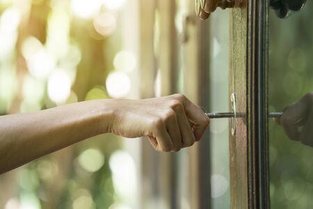 female hand putting house key into front door lock of houseの写真素材