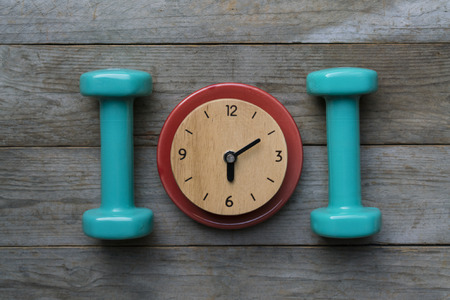 Time for exercising clock and dumbbell on the wood tableの写真素材