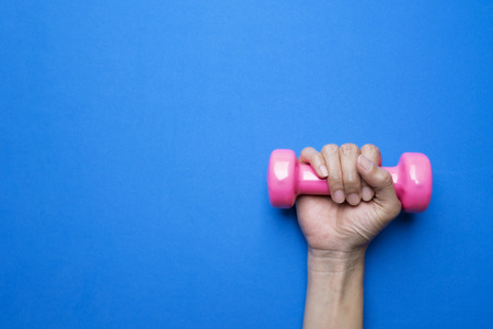 woman hand holding pink dumbbell on blue background, sport and healthy lifestyle conceptの写真素材