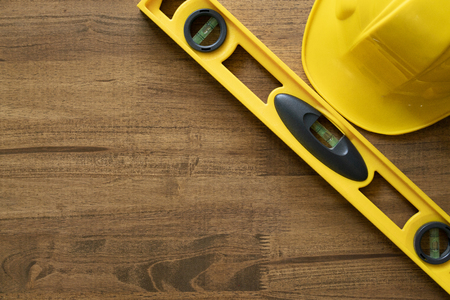 Yellow building level and yellow helmet on the old wood table, engineering work tool concept