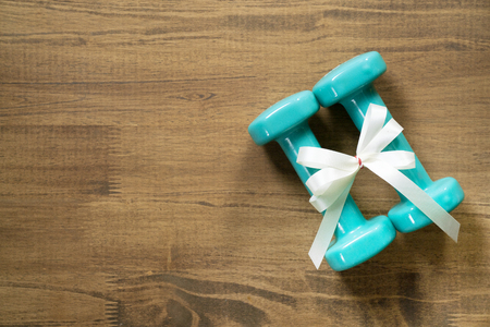 two green dumbbell with white gift bow on a table background, sport and healthy conceptの写真素材
