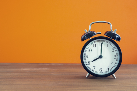 Retro alarm clock on wooden table with orange color background, vintage styleの写真素材