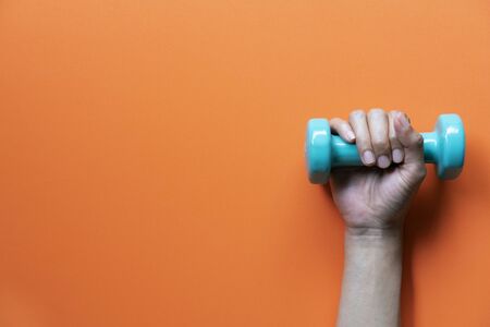 woman hand holding green dumbbell on orange background