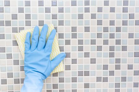 Cleaning tile wall by woman hand with glove, ready to clean house on bathroom backgroundの写真素材