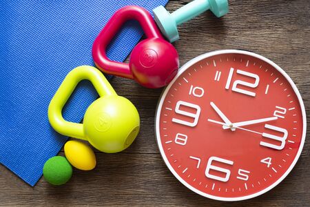 Time for exercising clock and dumbbell and sport equipment on wooden table backgroundの写真素材