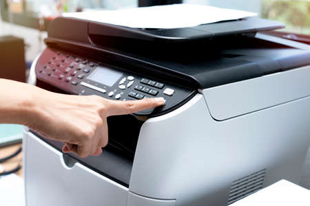 woman hands putting a sheet of paper into a copying device or printer in the office