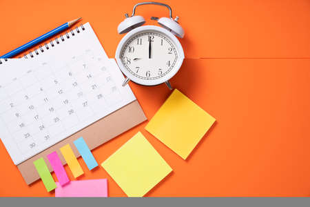 close up of alarm clock and calendar on the orange table background, planning for business meeting or travel planning conceptの写真素材