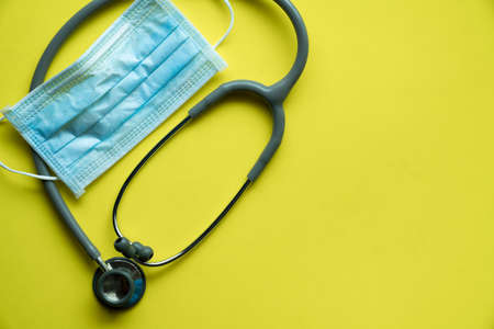 Medical disposable face mask and stethoscope protect from covid-19 or coronavirus on yellow table background, healthy and medicine conceptの写真素材