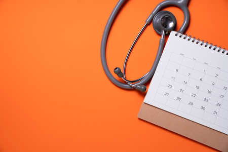 Top view of stethoscope and calendar on the orange background, schedule to check up healthy conceptの写真素材