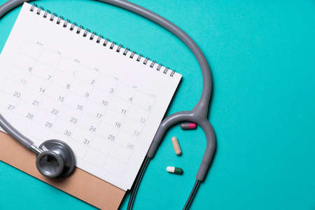 Top view of stethoscope, drug and calendar on the green background, schedule to check up healthy...