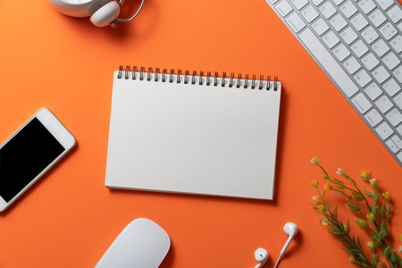 close up of workspace desk with smartphone, notebook, laptop or computer keyboard with copy space orange background, minimal style, for creative flat lay conceptの写真素材