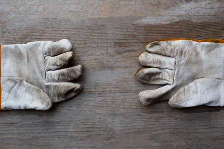 close up old dirty leather work gloves on wood background, engineering equipment concept