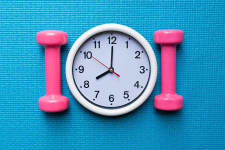 Time for exercising clock and dumbbell with blue yoga mat background, sport and healthy conceptの写真素材