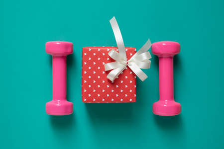 Dumbbells with red gift box on a green table background, sport and healthy conceptの写真素材