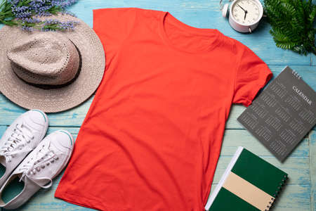 Mockup of a red t-shirt blank shirt template with accessories on the blue wooden table background,...