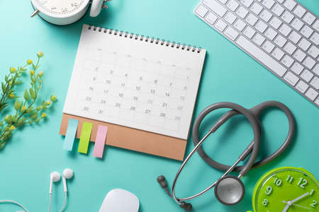 close up of calendar, computer and stethoscope on the green table background, planning for healthy and doctor meeting conceptの写真素材