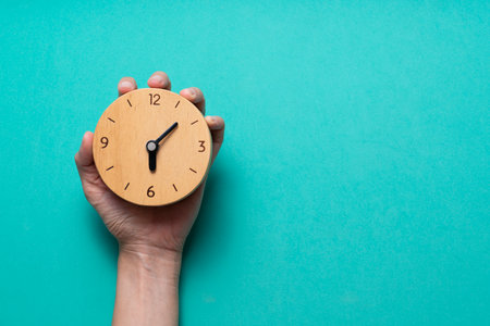 Hand of woman holding retro alarm clock on green table background, vintage styleの写真素材