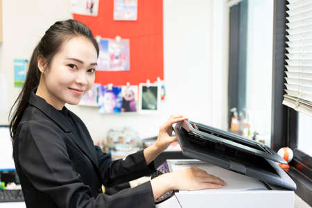 woman hands putting a sheet of paper into a copying device or printer in the officeの写真素材