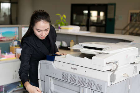 woman hands putting a sheet of paper into a copying device or printer in the officeの写真素材
