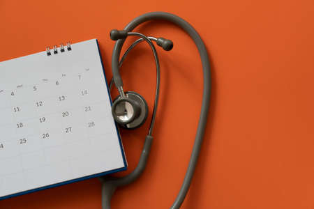 Top view of stethoscope and calendar on the orange table background, schedule to check up healthy conceptの写真素材