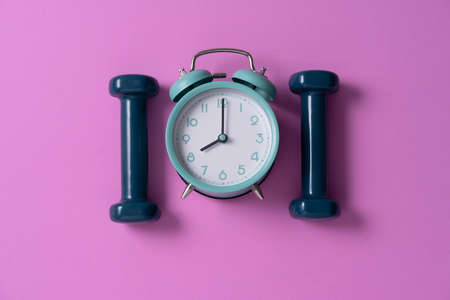 Time for exercising clock and dumbbell with pink background, sport and healthy concept