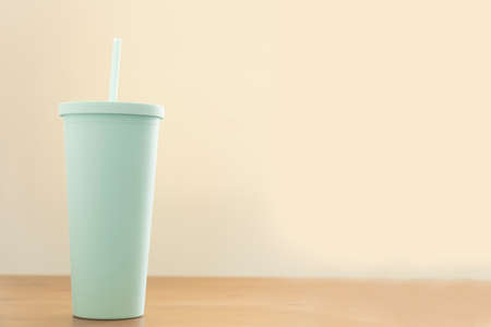 Close up of green cup or glass plastic and straw on wooden table. drink or beverage concept