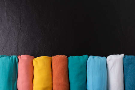 close up of rolled colorful t shirt clothes on black table background, travel conceptの写真素材
