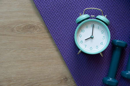 Time for exercising clock and dumbbell with purple yoga mat background, sport and healthy conceptの写真素材