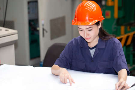 Portrait of a young woman Asian engineer smiling confidently while reading blueprints in a factory office, engineering technology conceptの写真素材