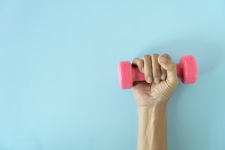 woman hand holding pink dumbbell on blue table background, sport conceptの写真素材