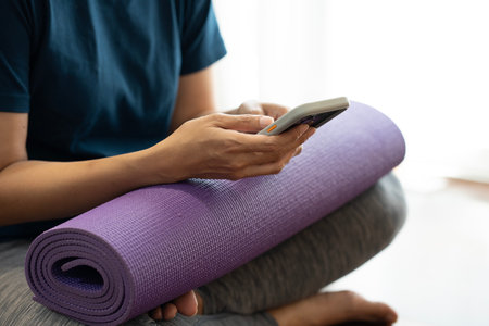Young woman holding a yoga mat and use the smartphone in exercise class, sport and healthy concept