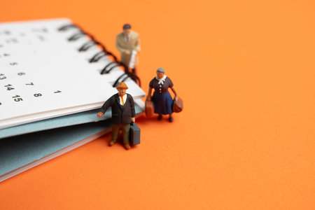 Miniature model people, travelers standing with the calendar on orange table background, traveling and planning conceptの写真素材