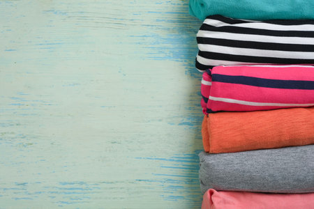 close up of rolled colorful t shirt clothes on blue table background, travel and lifestyle concept