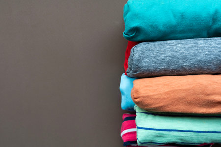 close up of rolled colorful t shirt clothes on brown table background, travel and lifestyle concept