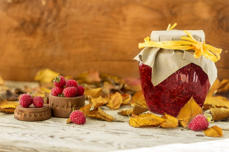 Autumn red and yellow leaves with raspberry jam on the wooden background