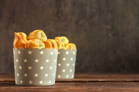 Eclairs or profiterole in gray paper cup with stars on wooden background. Traditional French dessert. Empty space for design text template.の写真素材