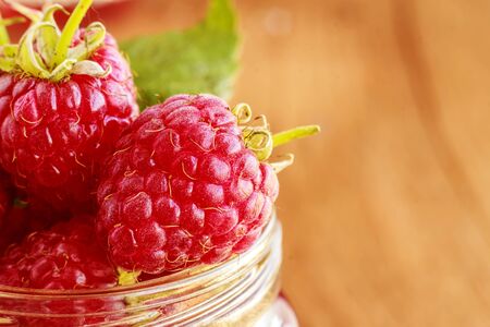 Fresh ripe raspberry in glass bottle on brown background. Copy space. Close up. Front view.