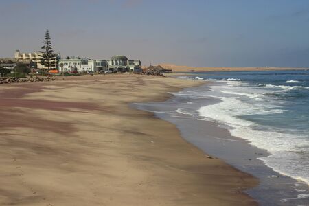 Beautiful pink sand on the shores of the Atlantic Ocean, waves and stones on a sunny bright day. Swakompund, Namibia.の写真素材