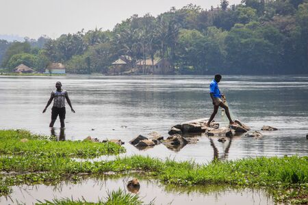 Jinja, Uganda - January 20, 2015: African men cross the rocks at the source of the great and longest river Nile.のeditorial素材