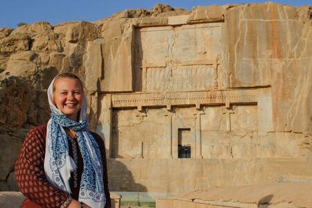 White young woman tourist with a head covered stands on the background of the famous bas-reliefs of the day capital of Persia (Iran) - Persepolisの写真素材